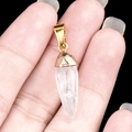 Faceted clear amethyst quartz bullet pendant with a gold-plated cap held by fingers - White Crystal