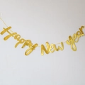 Detail of metallic gold Happy New Year banner letters hanging on a white wall - Cursive Gold