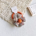 Detailed close-up of floral fabric flower hair tie with soft orange pompom on display card - Orange Floral