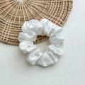 Detail of white satin scrunchie with silky texture and folds on a woven rattan mat - Medium White