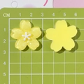 Top-down view of yellow resin cherry blossom charms on a green centimeter scale mat - Yellow