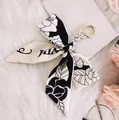 Detail of camellia floral silk bow keychain with gold metal clasp on plush background - No.1 (Black and White Floral)