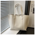 Detailed view of a cream-colored minimalist tote bag placed by a window in a bright room - White