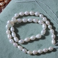 Strand of 5-6mm natural white oval freshwater pearls on green velvet background - White