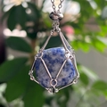 Close-up of a blue natural stone pendant secured in a silver mesh cage necklace - Sodalite