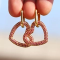 Orecchini a cuore dorati con zirconi rosa incastonati mostrati in un primo piano - Rosa Rossa