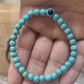 Detail eines Perlenarmbands aus Türkis mit zentralem blauem Evil Eye Anhänger - 6mm / Türkis