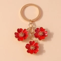 Détail d'un porte-clés doré orné de trois fleurs de pêcher en émail rouge élégant - Rouge
