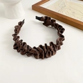 Détail d'un serre-tête en tissu plissé marron foncé sur un décor de table minimaliste - Marron