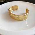 Detailopname van een vintage gouden open armband met bloemenpatronen op witte ondergrond - Goud