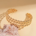 Dettaglio di un bracciale rigido dorato a tre file di perle con design minimalista - Oro