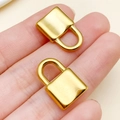 Deux pendentifs cadenas cœur en acier inoxydable doré tenus en main pour bijoux DIY - Grande serrure concave