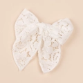 Dettaglio di un fermaglio per capelli a fiocco in pizzo bianco con ricamo floreale su sfondo beige - Bianco