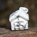 Detailed view of hand-carved white turquoise stone house miniature on rustic wood base - Howlite