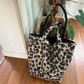 Detail of plush leopard print tote bag with metal label on wooden floor and green plant - Leopard Plush Style