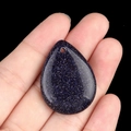 Teardrop-shaped blue sand stone pendant with shimmering specks held in hand - Blue Goldstone (Synthetic)
