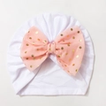 Detail view of baby turban hat in white knit fabric featuring a large pink gold polka dot bow - White with Bud Green Bow