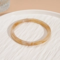 Detalle del brazalete de resina ámbar con textura de mármol sobre un plato de cerámica blanca - Estilo de Borde Delgado con Textura de Mármol Blanco Arroz