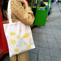 Close-up of white canvas tote bag with yellow lemon print worn on shoulder outdoors - Lemon