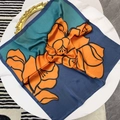 Floral silk scarf with orange flowers on blue background on white marble table - Teal