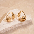 Detail of twisted gold metal earrings with a spherical drop on a natural stone base - Gold