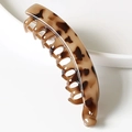 Macro detail of the leopard print resin banana hair clip on a white ceramic edge - Cream Amber