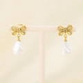 Close-up of golden bow earrings with baroque pearls and zircon inlay on pink stand - Gold Bow Rhinestone (KE115976-GC)