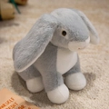 Soft grey and white lop-eared bunny plush toy sitting on a beige rug in a cozy room - Grey Rabbit