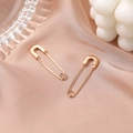 Minimalist golden safety pin earrings displayed on elegant peach silk fabric background - KC Gold Pin Earrings (DZ-340)