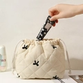 Quilted beige cosmetic pouch with butterfly embroidery being used for skin care storage - White with Bowknot