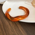 Macro detail of amber resin bangle with irregular wave design on a ceramic plate - Amber