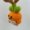Detail of hand-crocheted carrot doll holding a card with caring pun message - Chubby Carrot