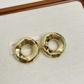 Gros plan de boucles d'oreilles dorées texturées sur un présentoir à bijoux minimaliste - Type G Créoles Irrégulières Dorées