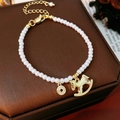 Detailed close-up of pearl bracelet with golden pony and coin charms on a jewelry box - Bracelet - Gold - White