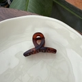 Detailed view of a brown tortoiseshell hair claw clip placed on a white ceramic dish - 5.5cm Butterfly Buckle / Matte Red Brown