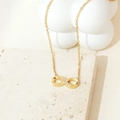 Vue détaillée du collier infini doré avec zircons sur un support en travertin naturel - Or Infini avec Micro-pavage de Zircone