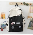 Detail of a black and white nylon backpack with cute cartoon badges hanging on a wooden hook - Single Bag / Black & Beige