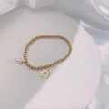Close-up of golden beaded bracelet with pearl and sun charm on a ceramic display - Gold - Sunburst