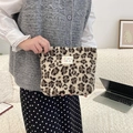 Detailed view of a plush leopard print makeup bag held against a cozy indoor background - Beige Leopard