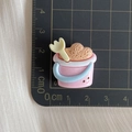 Detailed view of pink resin sand bucket accessory with blue handle on a grid cutting mat - Pink Bucket