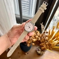 Quartz watch with a beige faux suede strap and a clear round dial held by hand in soft light - Apricot