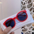 Close-up of red round kids sunglasses with dark lenses and a white leather case - Red Frame Grey Lens