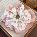 Detail view of a white scrunchie with pink bow pattern and lace trim in a wooden box - White Fabric Pink Bow Lace Edge