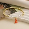 Vista detallada de la pulsera de cuentas doradas, perlas blancas y un colgante de coral - Naranja