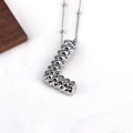 Macro shot of silver L-shaped letter pendant with embossed rivet texture and metal finish - L