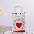 Dettaglio della borsa in maglia crema con cuore rosso e scritte artistiche in blu - Bianco Sporco