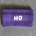 Detail eines lila gestrickten Sportstirnbands mit weißem HO-Patch und Rippenstruktur - Lila