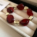 Close-up of deep red resin beads and polished gold metal beads on a beige velvet tray - Red