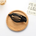 Matte black fish-shaped hair clip with interlocking teeth on a wooden tray - Matte Black