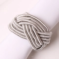 Close-up of silver woven knot napkin ring on white fabric with detailed texture - Gray